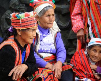 A group of Indigenous people in traditional clothing kneeling and sitting around each other