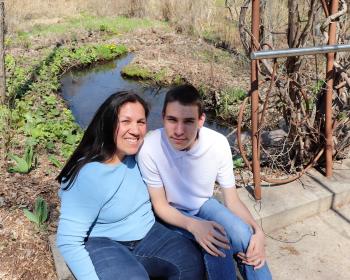 Margaret King and son Hudson Francour sitting by a creek, smiling