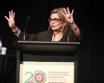 Pat Dudgeon standing behind a podium, speaking to an audience