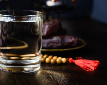 Photo depicts a glass of water and prayer beads on a table