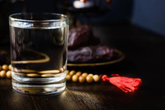 Photo depicts a glass of water and prayer beads on a table